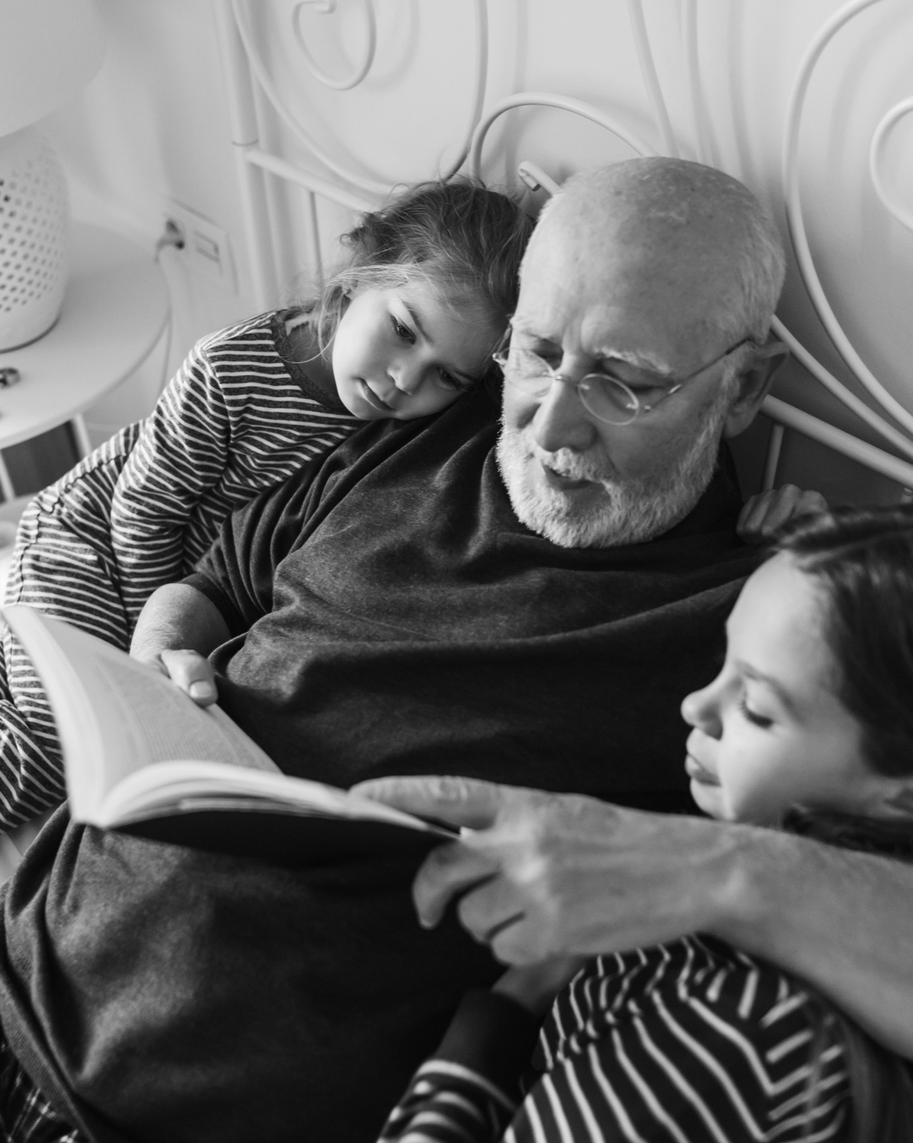 A grandfather reading a book in bed with two children beside him